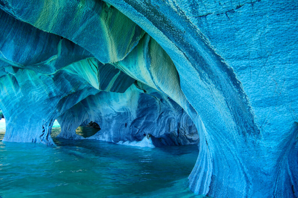 Blue marble caves in Patagonia with light selectively illuminating sculpted surfaces while deeper formations remain in shadow — AI that reveals what it can determine and honestly acknowledges what it can't