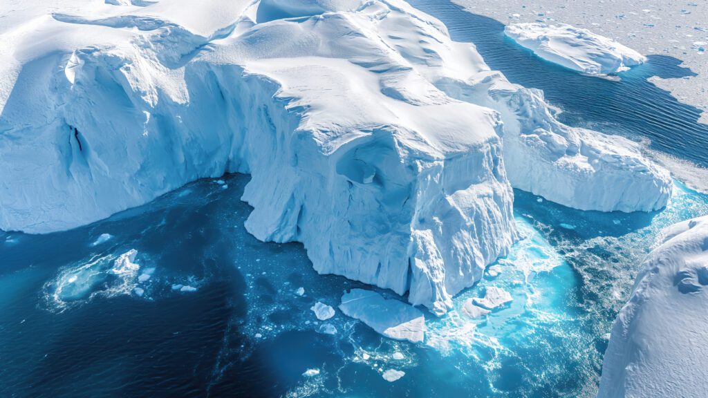 Aerial view of a massive Antarctic iceberg — the visible surface impressive, the submerged structure beneath the turquoise water vastly larger.