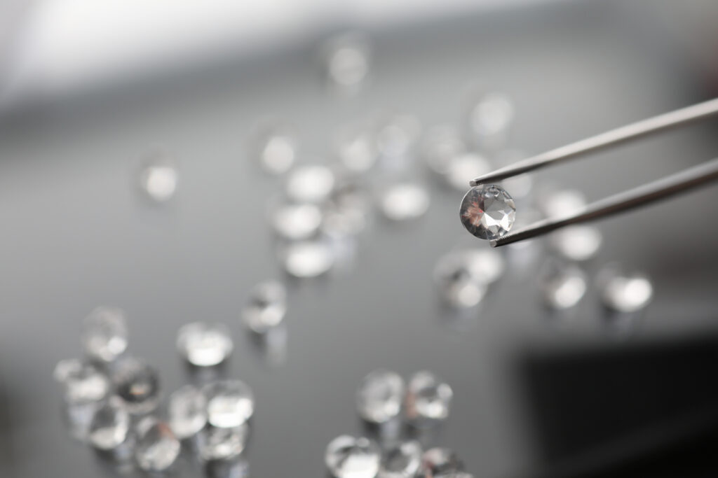 A single diamond held in sharp focus by jeweler's tweezers, with many similar diamonds blurred in the background — representing how retrieval architecture selects the right context from thousands of options before an AI model ever sees it