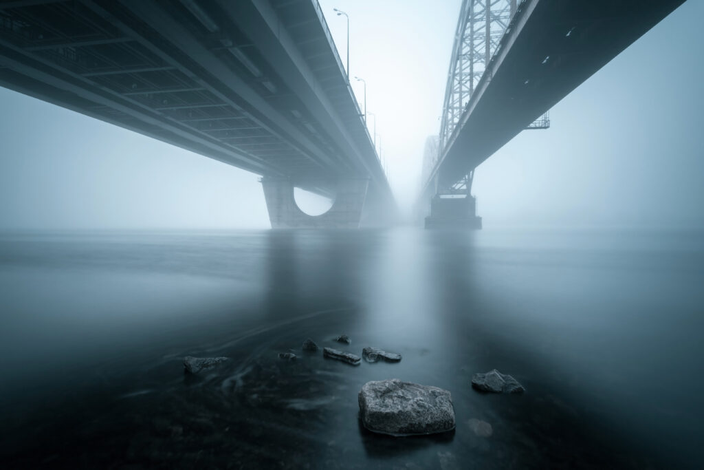 Two parallel bridges stretching over a foggy river — representing the deliberate decision to build architectural independence by constructing the same system twice on different foundations